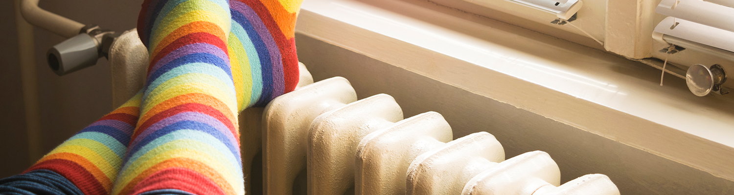 Pair of legs in long, colourful striped socks crossed on top of a radiator next to a window.