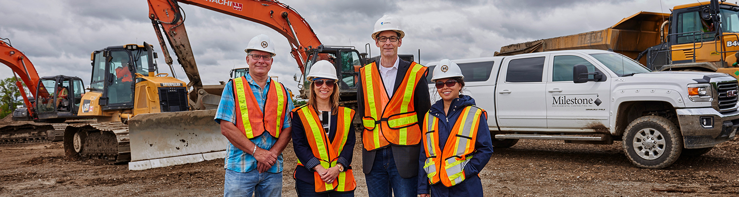 The project team smiles for the camera on the brownfield site, with construction equipment and a pickup truck in the background