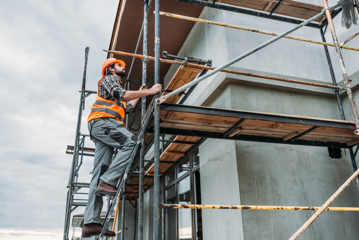 Builder in orange safety vest climbs scaffolding