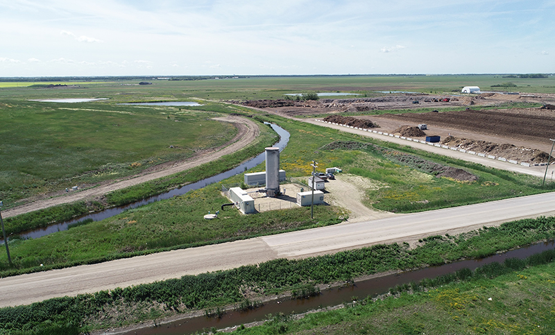 Aerial view of a waste management facility situated in a large grassy plain near a small river. 