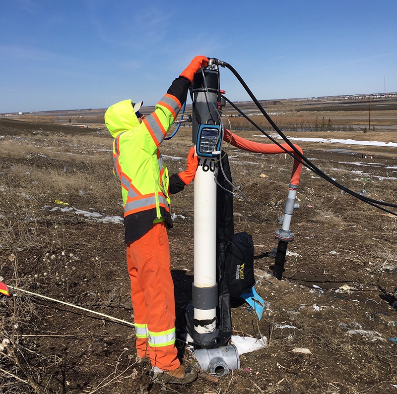 Municipal employee in orange safety gear insects a gas collection well in the center of a field in spring. 