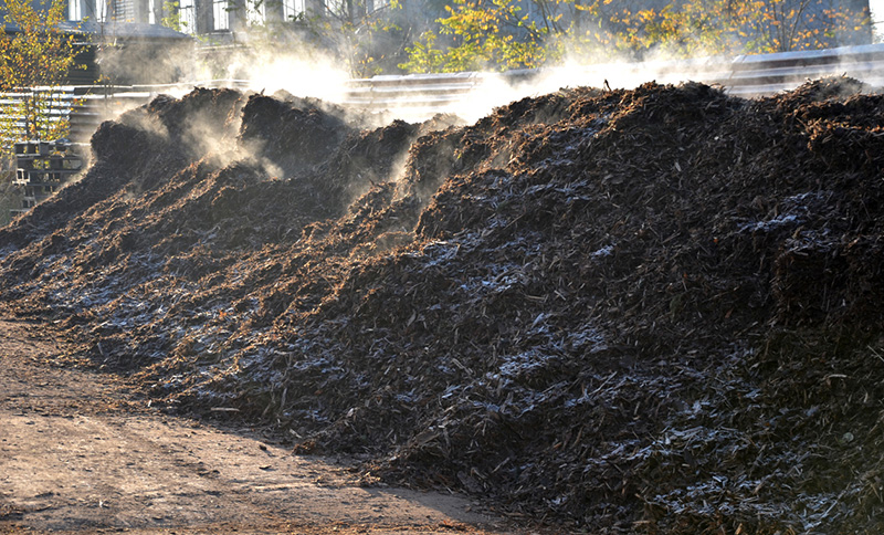 Pile of brown compost releases steam in the morning