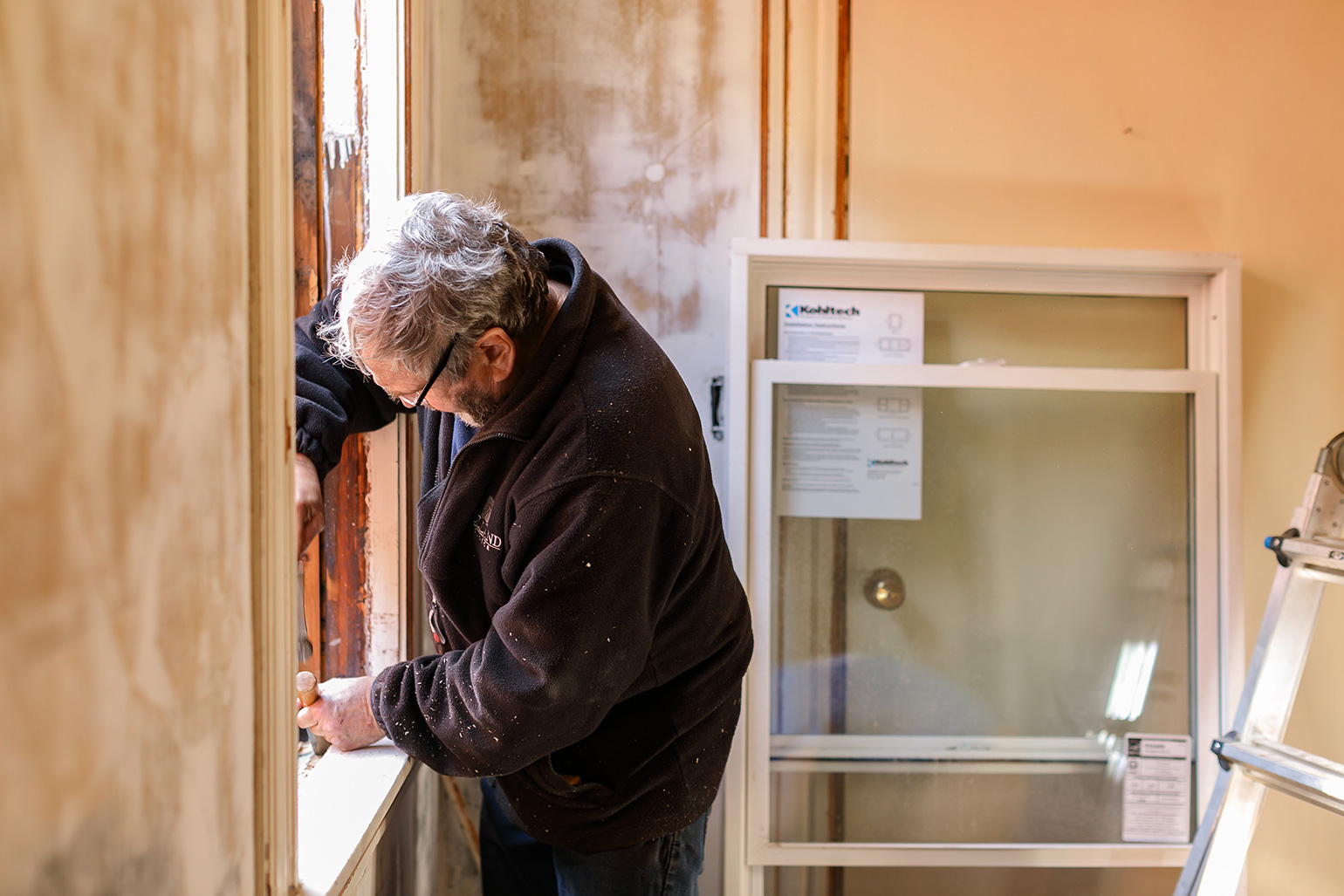 A side view of a man removing a window inside a home for a retrofit