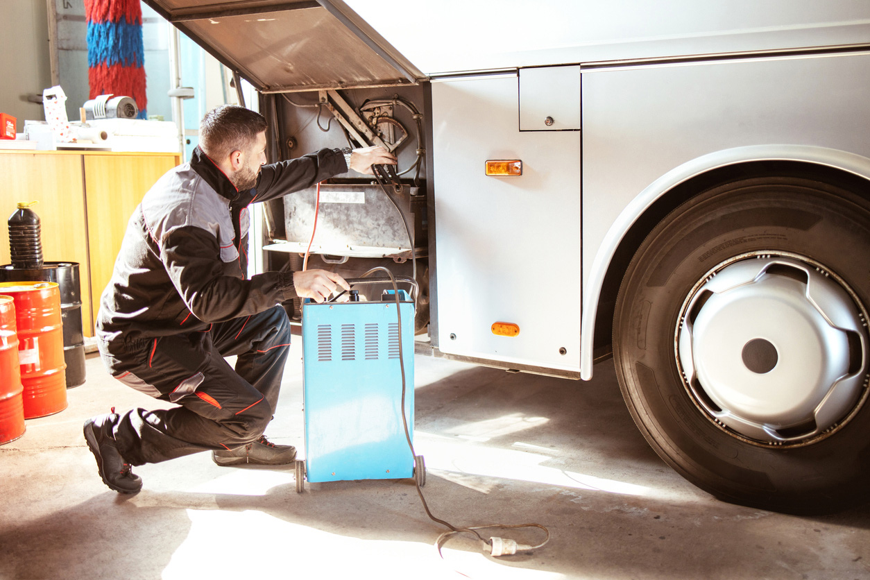 Electrification in a sunny garage charges an electric bus with a portable battery. 