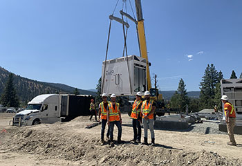A group of workers in safety equipment poses and smiles at a construction site in front of a truck lowering a battery energy storage system