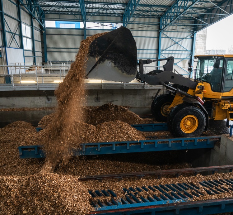 A tractor dumps biomass into a pile inside a storage facility