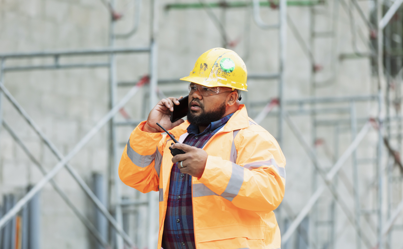 Construction worker outside talking on a cellphone in full safety gear.