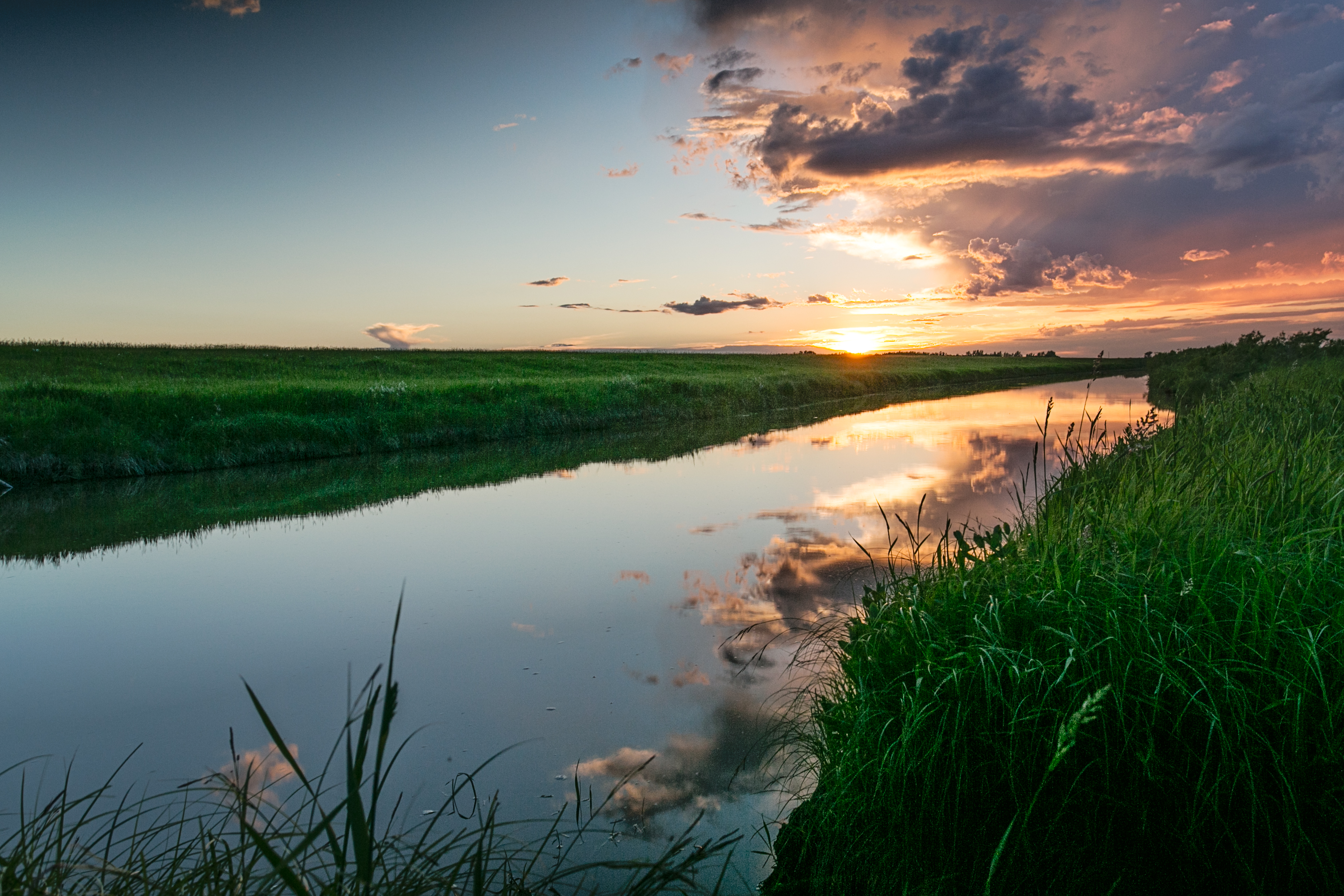 Sun sets over a grass-flanked river in Manitoba.