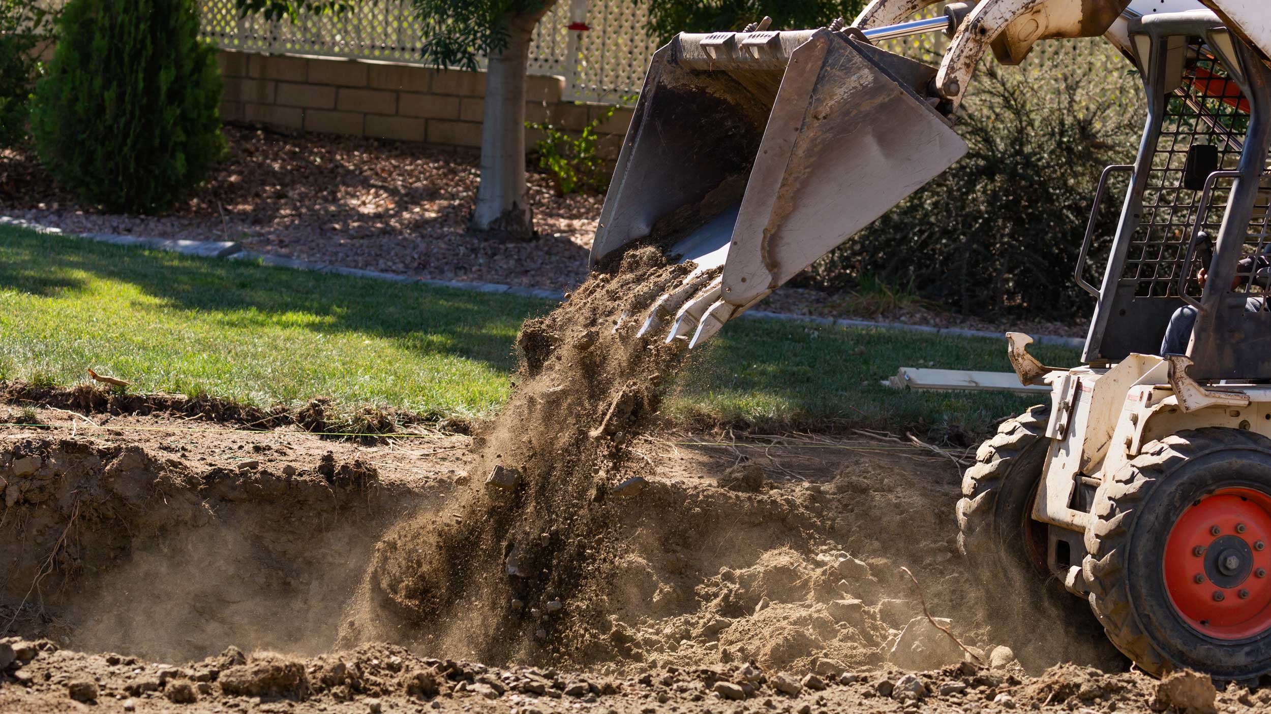 Small bulldozer digging in yard on sunny day.