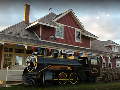 A red and white restored train station with a decorative black train in the foreground.