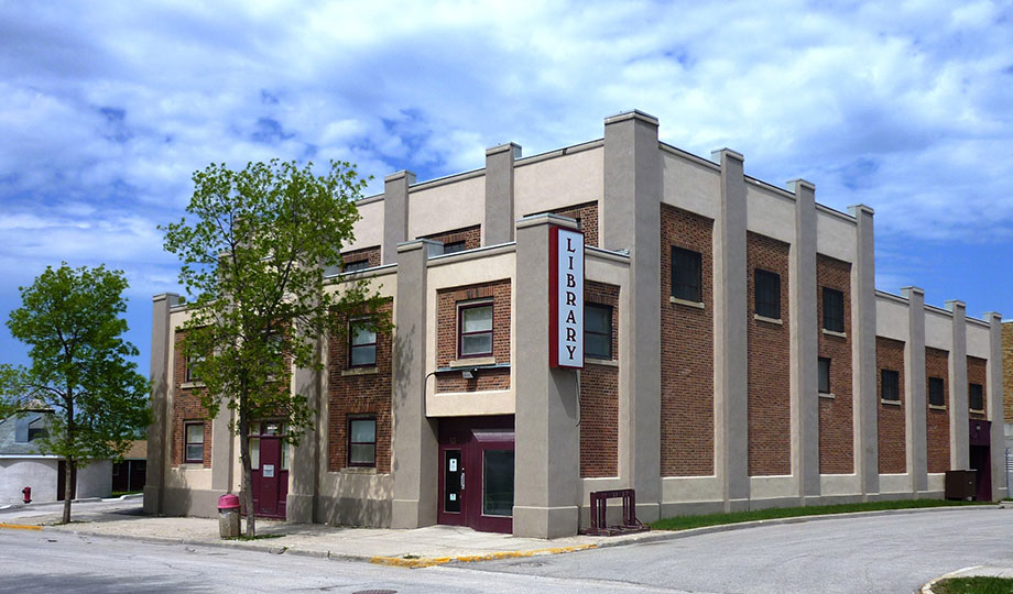 Front view of The Pas Regional Library, a red and beige brick building with two trees.