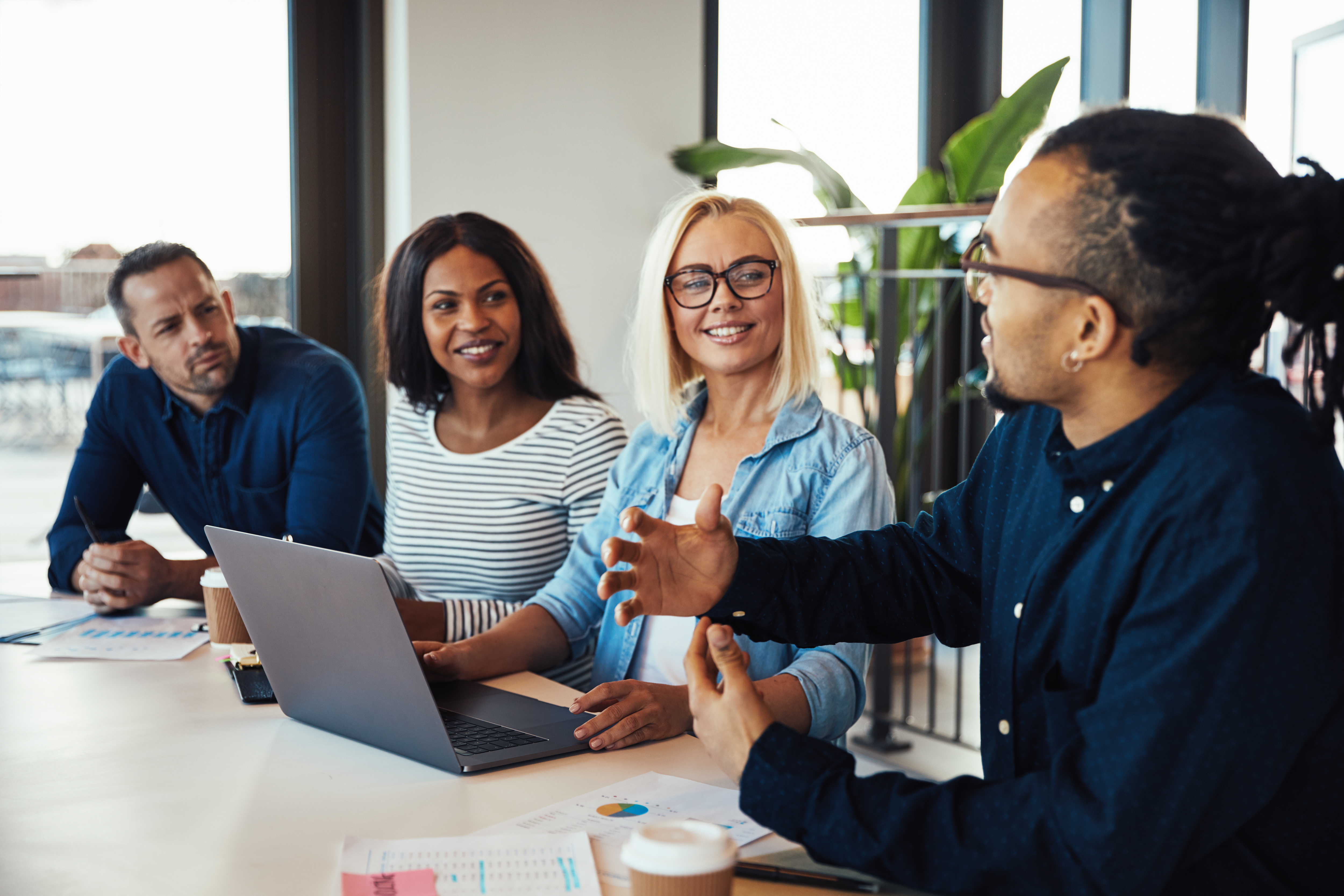 Four colleagues in a bright, modern office discussing business around a laptop. 