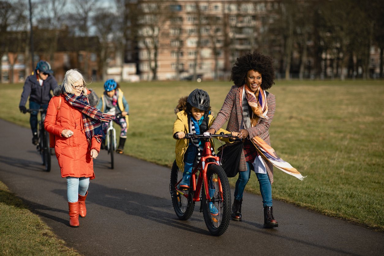 Group of children riding their bicycles through a city park, guided by their parents. 