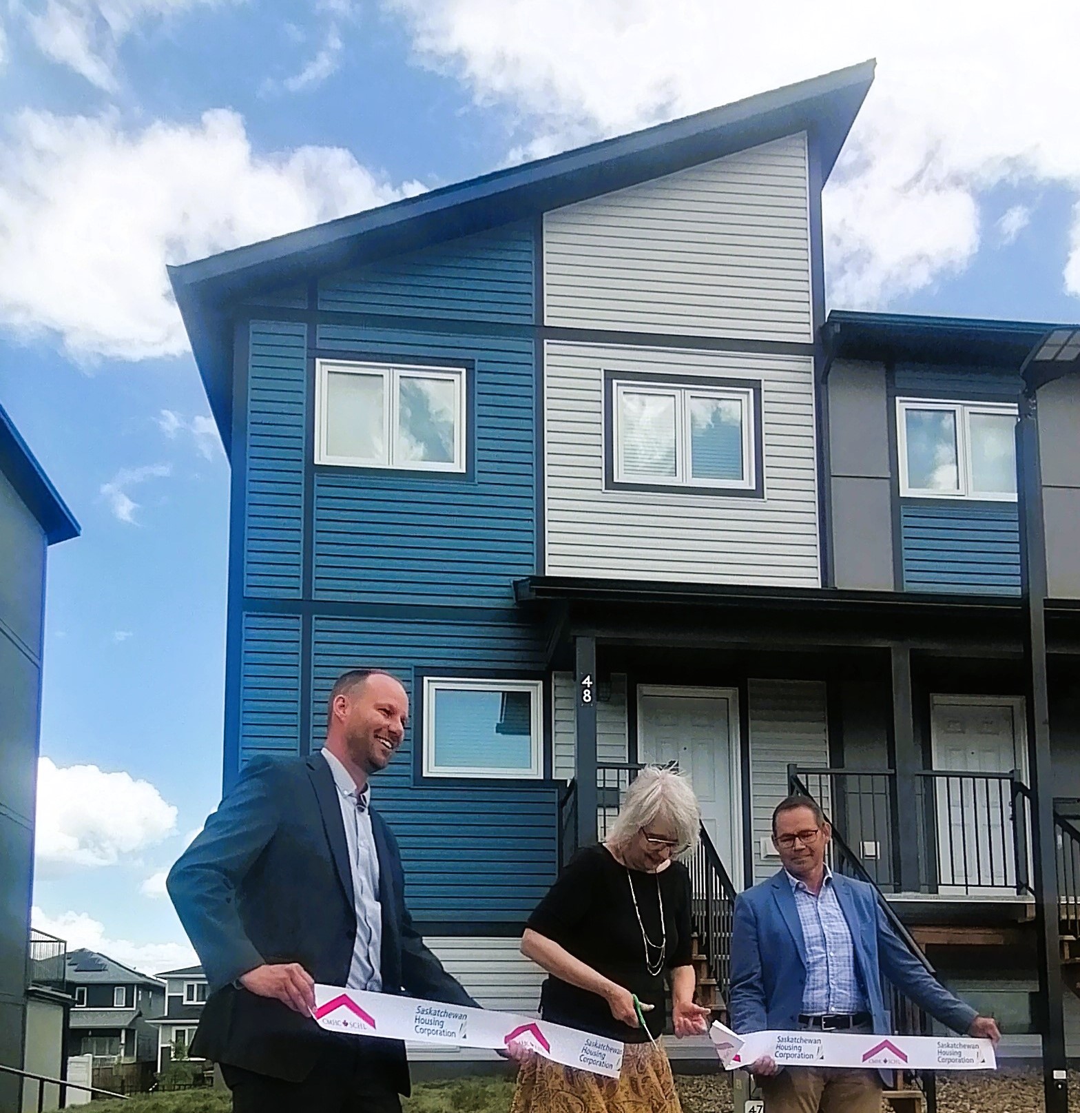 Three people cut a ribbon outside a home in the Aspen Heights development in Saskatoon. 