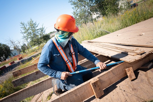 A construction worker, wearing an orange safety hat, is using a crowbar to pry apart large wooden panels.