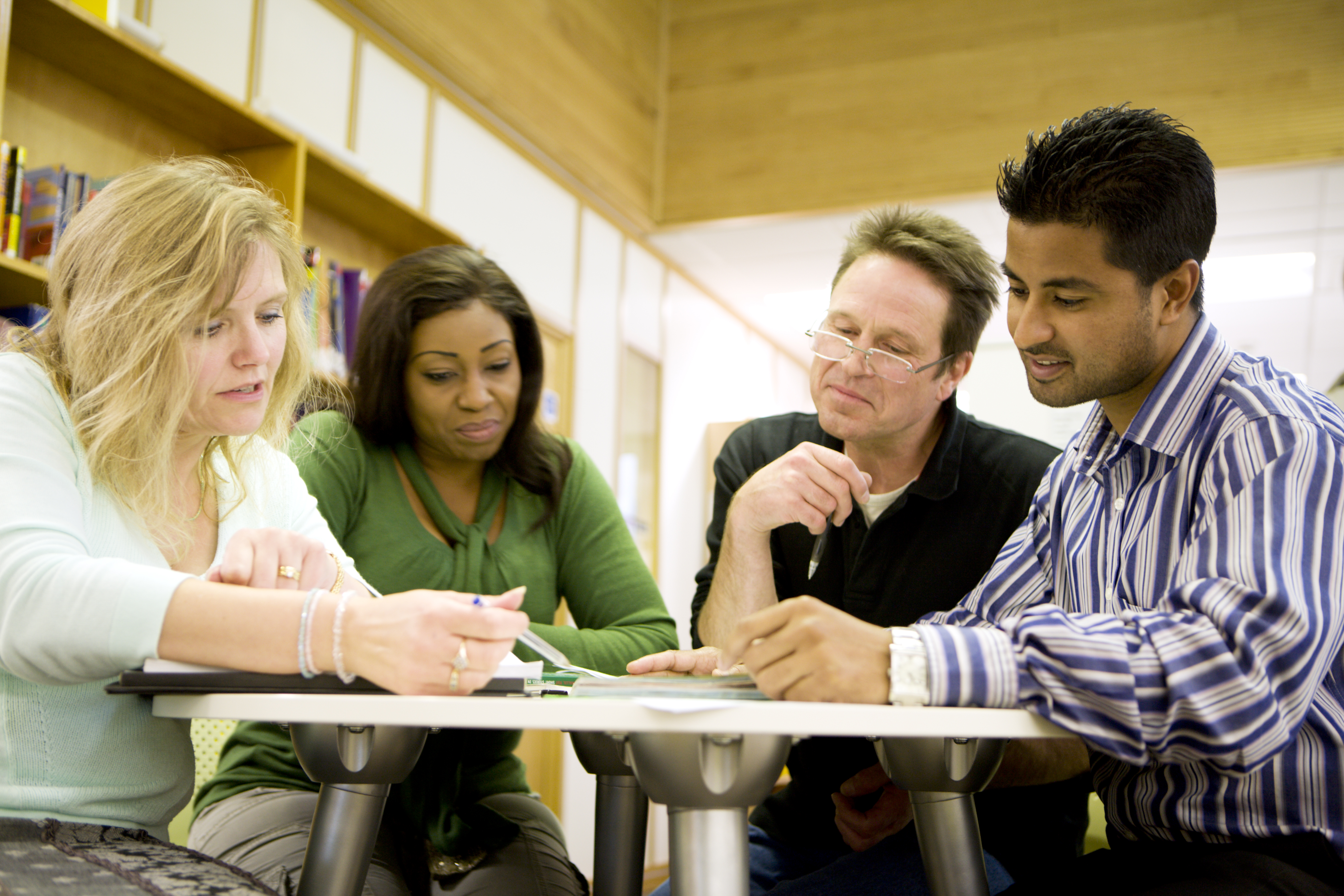 Four adults of diverse backgrounds collaborate around a table in a bright meeting room. 