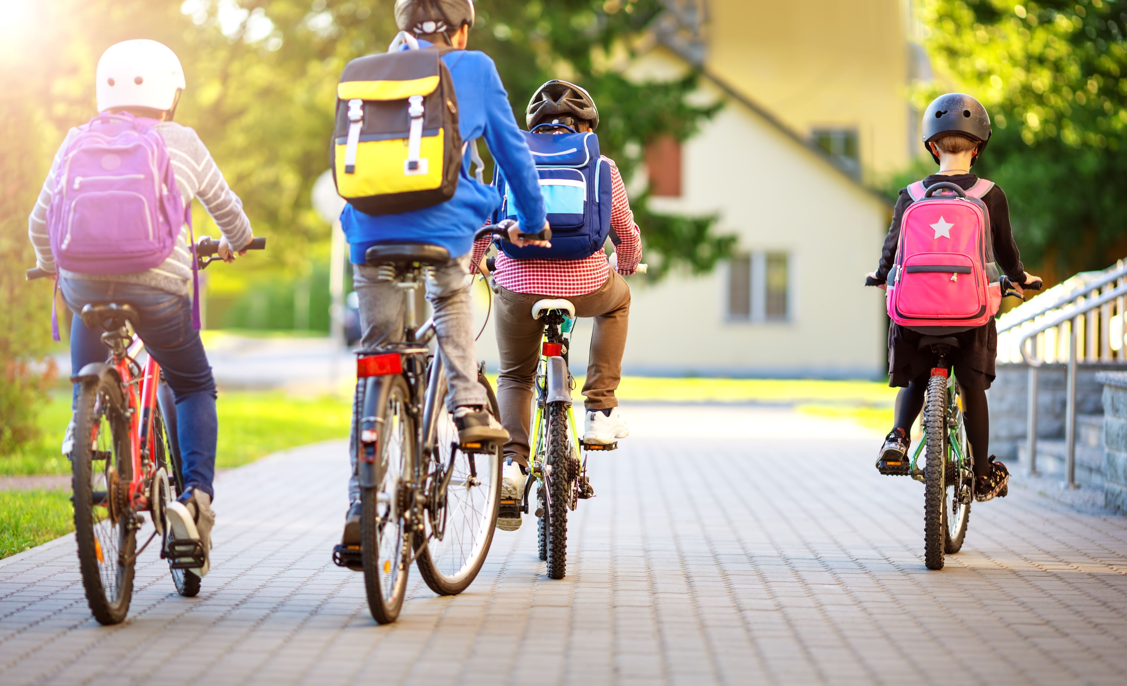 Children with backpacks riding bikes near a school