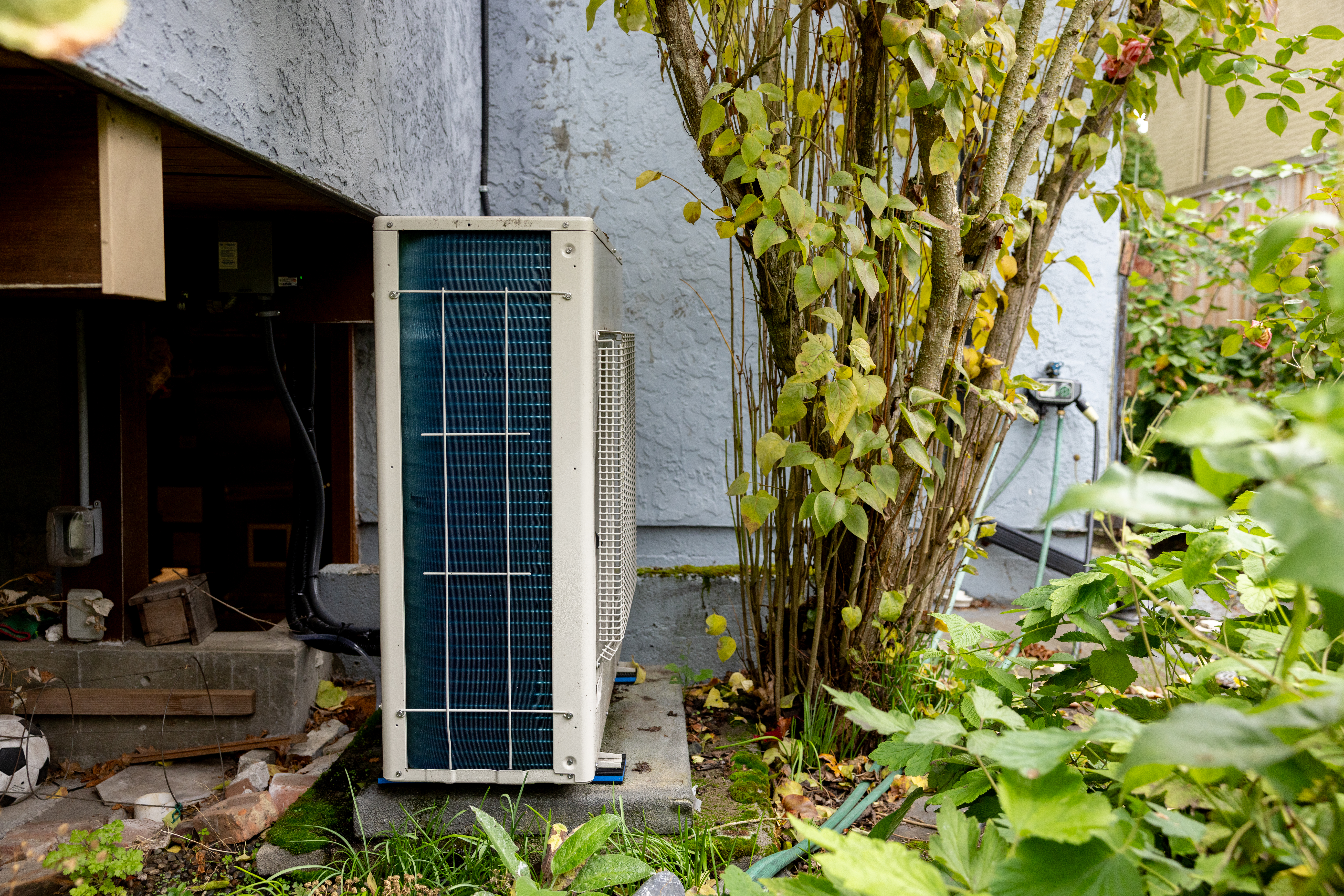 Close up of outdoor heat pump under some brush behind a house. 
