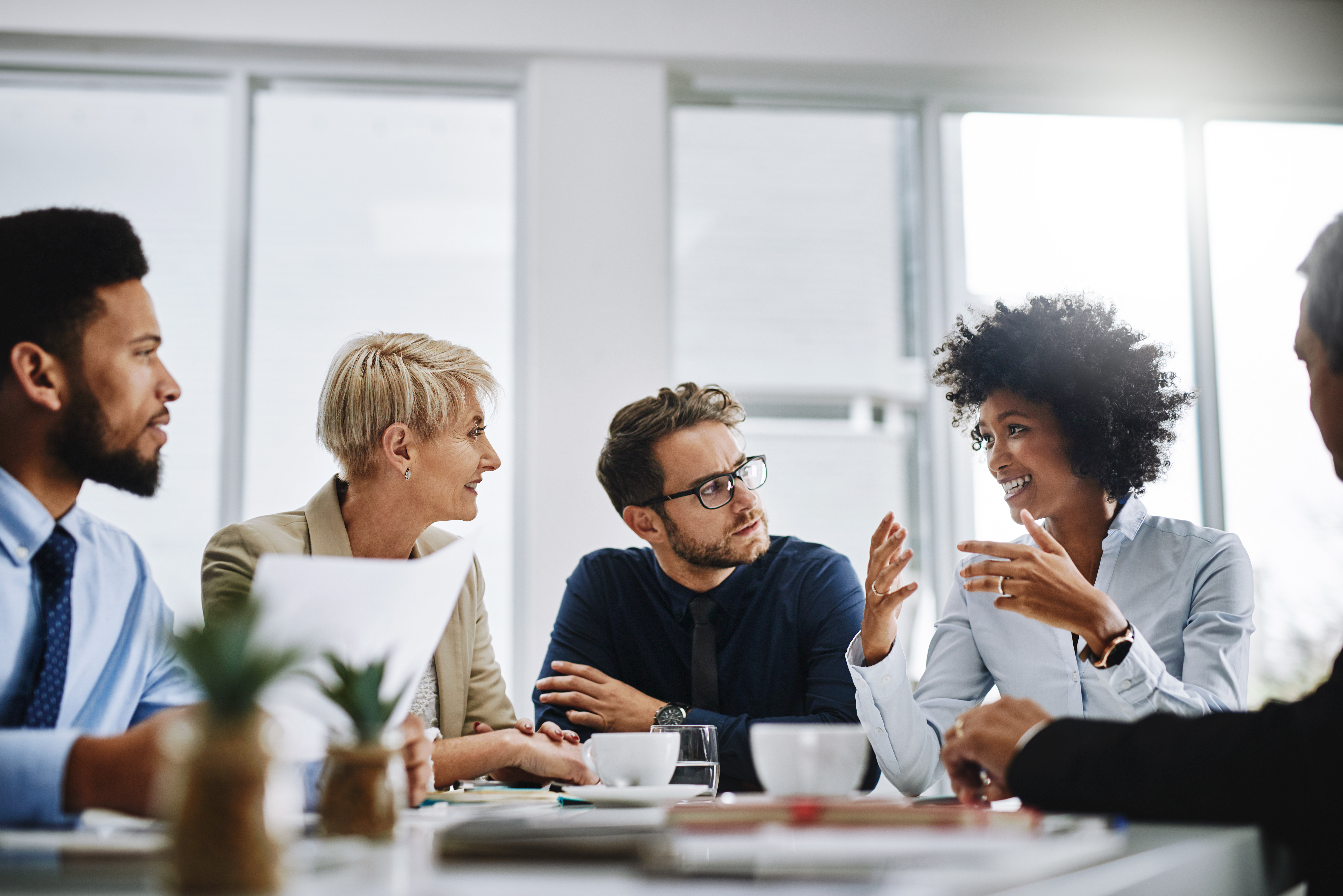A diverse group of professionals sitting together in a meeting room, discussing ideas and collaborating around a table.