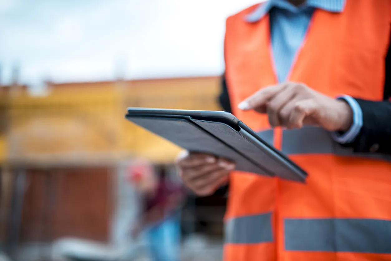 Engineer in orange safety vest using a tablet on the job site.