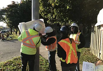 A group of construction workers gathered together outside, engaged in a discussion over a set of design plans