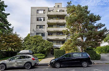 Side view of Brightside Community Home featuring a paved pathway leading to the entrance, two cars parked in front, and the building is nestled among hedges and trees