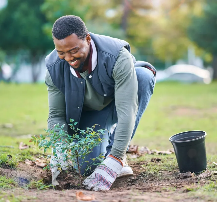 Smiling man plants a young tree in his community.