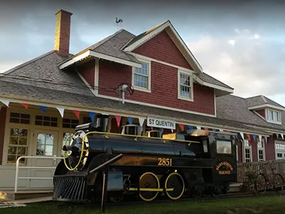 A red and white restored train station with a decorative black train in the foreground.