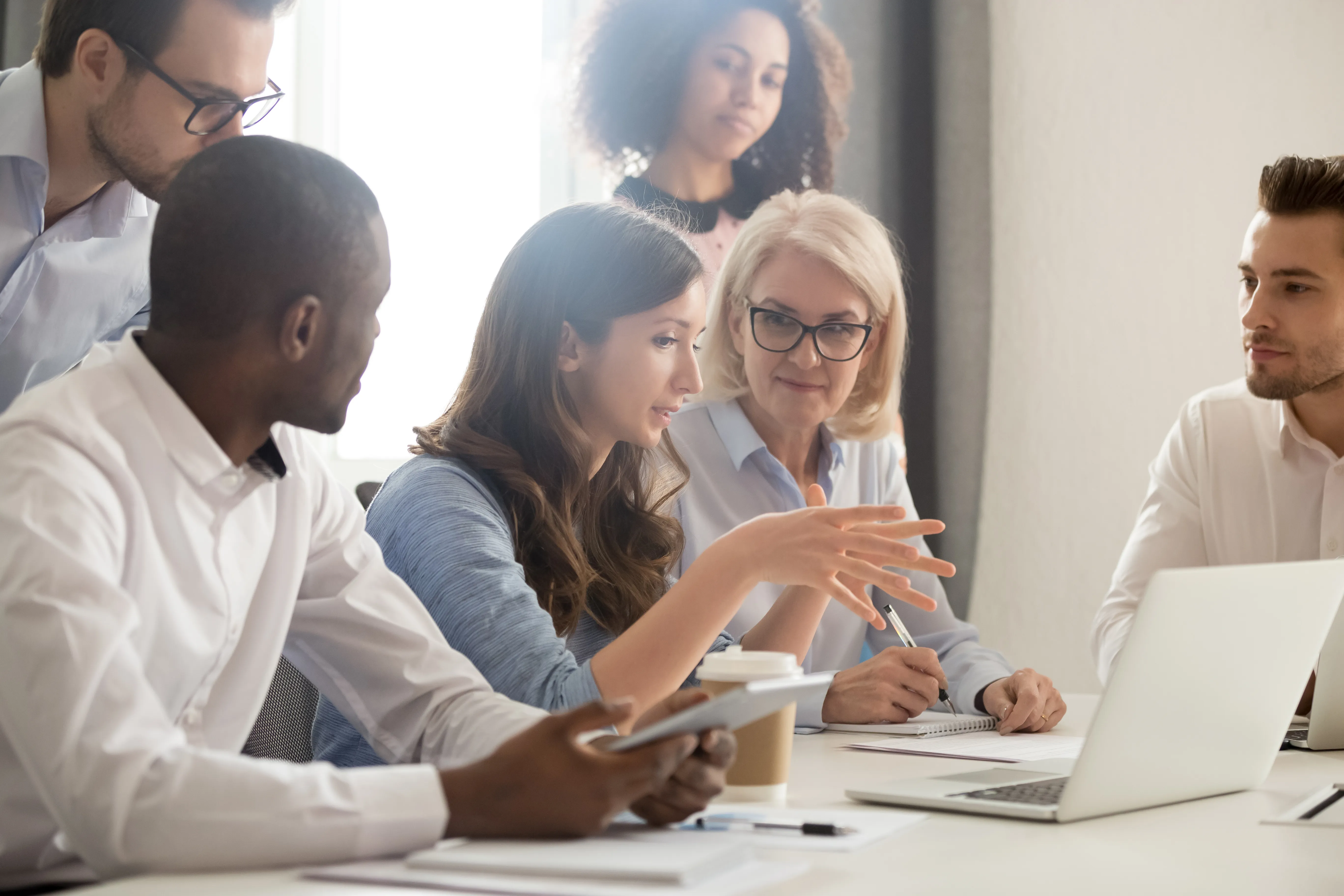 Diverse group of professionals in a discussion, with a woman leading the conversation and gesturing while others listen, representing teamwork and strategic planning