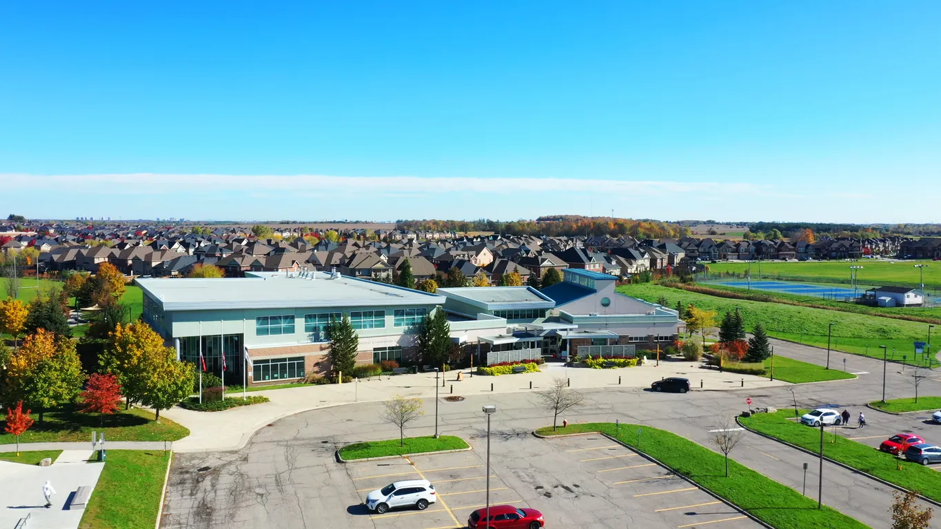 Aerial view of a modern community centre surrounded by homes, fall trees, and open green space under a clear blue sky. 