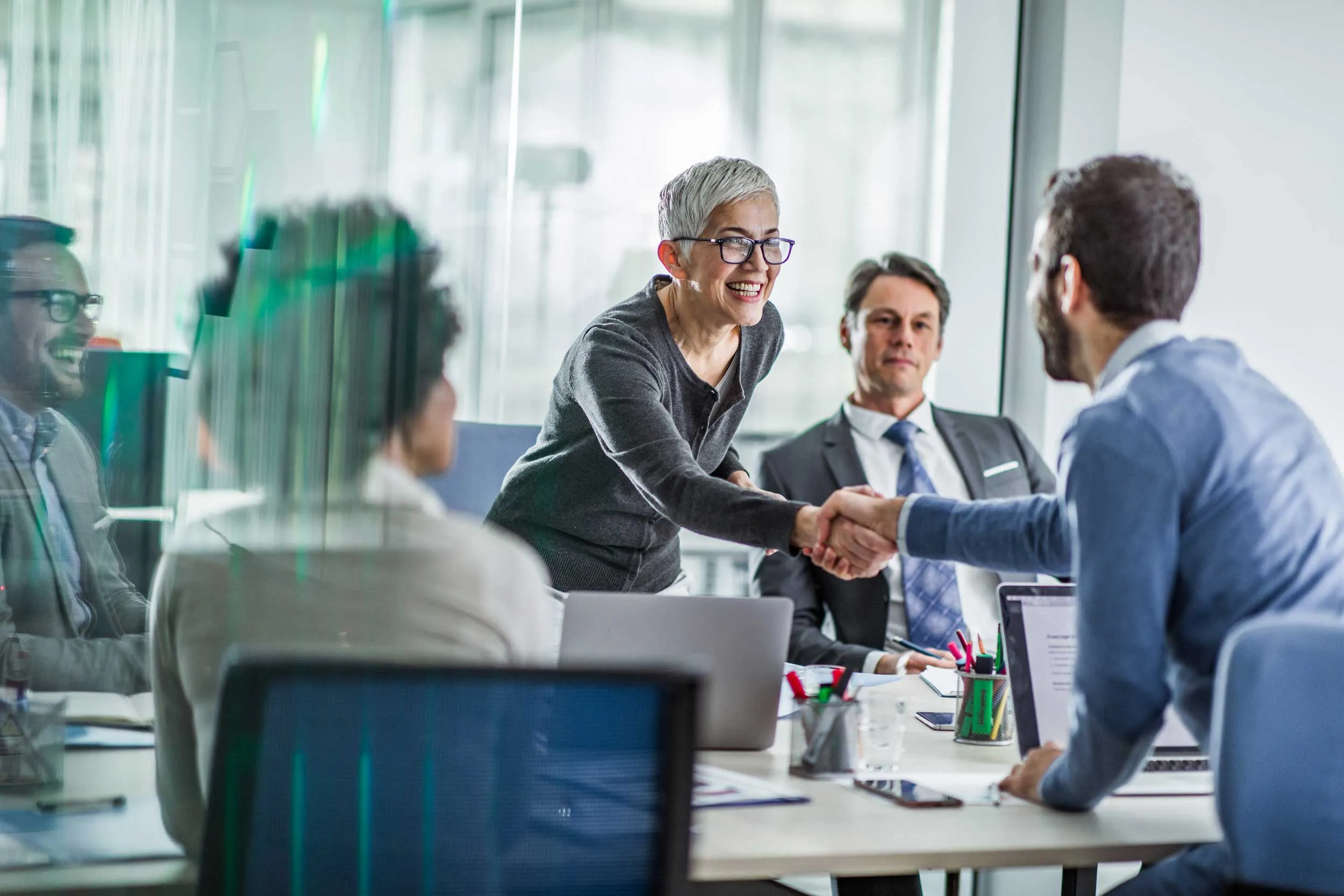 A group of professionals in a meeting room, one person smiling and shaking hands with another, symbolizing partnership and gaining council support.