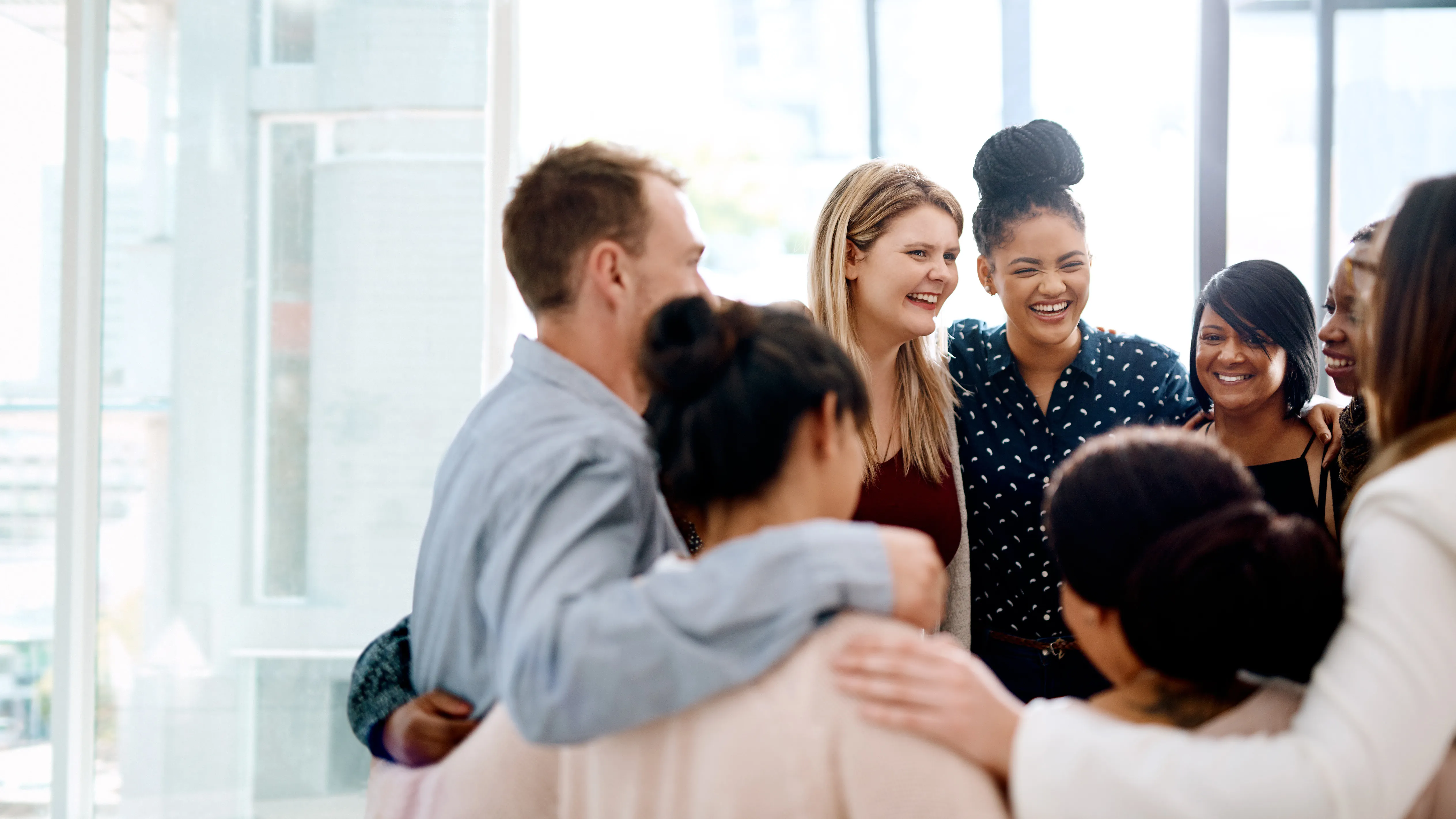 Group of colleagues standing in a circle, smiling and connecting in a team huddle, symbolizing collaboration and partnership.