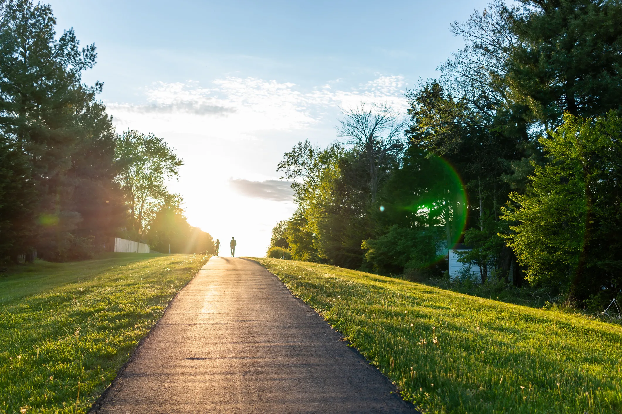 Person walking on a sunlit path through a green park, symbolizing progress and forward movement.