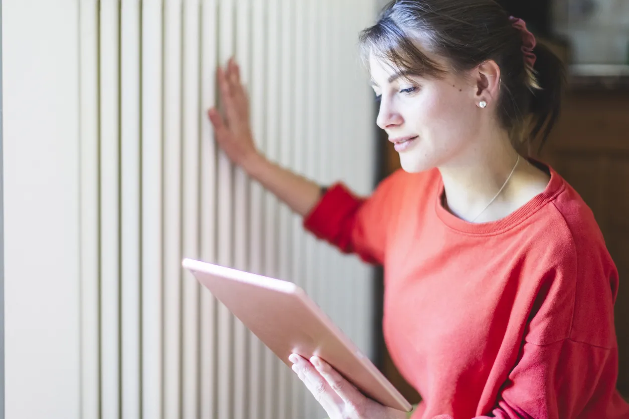 Young woman checking with radiators with device in bright living room. 