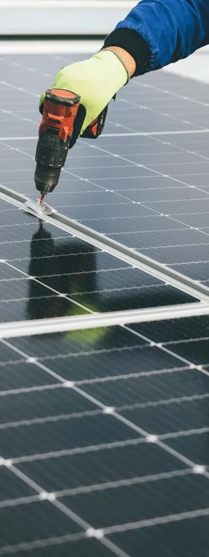 A hand with construction glove on using an electric screwdriver on a solar panel.